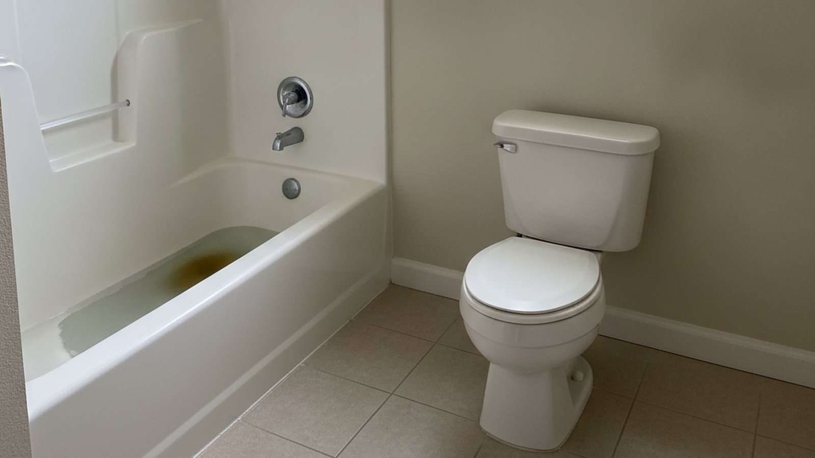 Ground-floor bathroom with murky backed-up water sitting in the bathtub beside a toilet