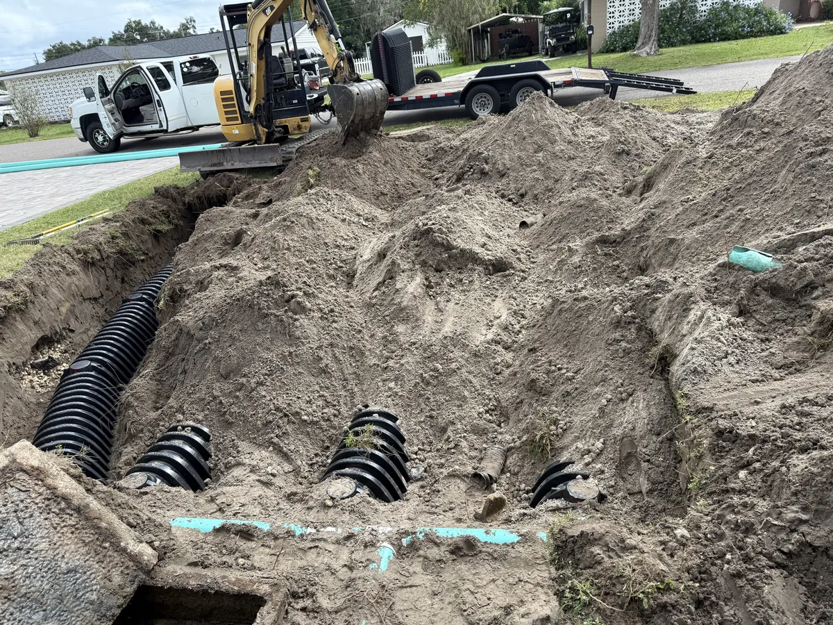 OC's Plumbing & Septic drain field restoration job site with excavator and exposed infiltrator chambers